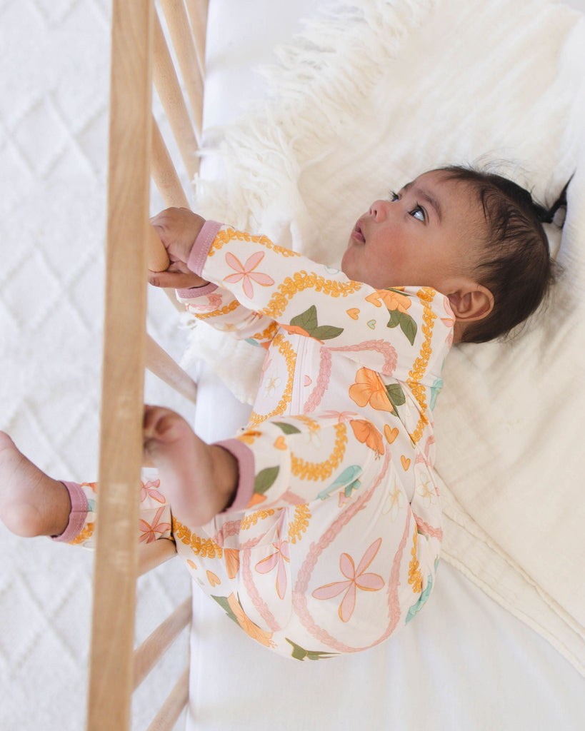 Baby in a crib with a floral outfit, surrounded by white bedding and wooden bars.
